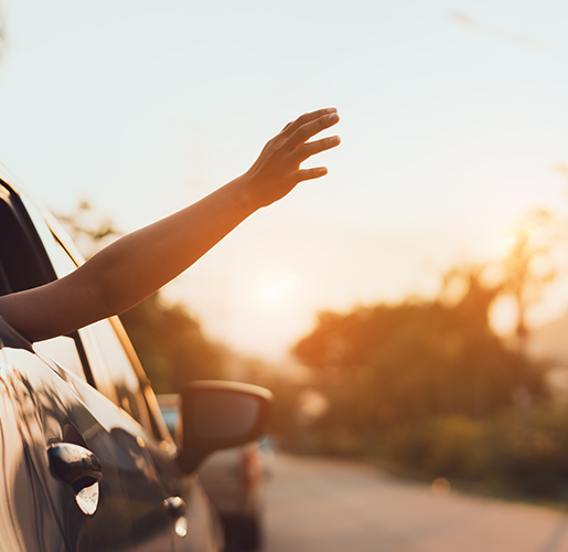 The image shows a person's arm extended out of the window of a car, reaching into glowing light of either sunrise or sunset