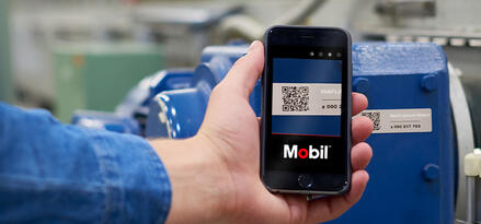 Technician using a mobile device to scan a QR code on industrial equipment with the Mobil interface displayed on the screen