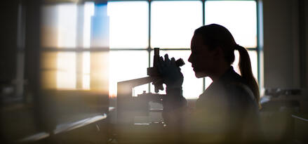 A woman looking into a microscope in a lab