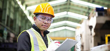 Construction worker wearing safety gear and writing on a clipboard inside an industrial facility