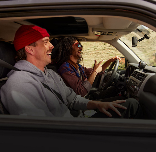 Two people sit in the front seats of a vehicle, viewed from the open rear door on the driver’s side