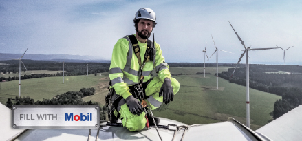 Technicien en équipement de sécurité sur une éolienne surplombant un parc éolien, avec un panneau Mobil au premier plan.