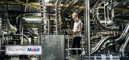 Personne utilisant une tablette pour inspecter des équipements de fabrication automatisés dans une installation industrielle. Le logo Mobil apparaît au premier plan.