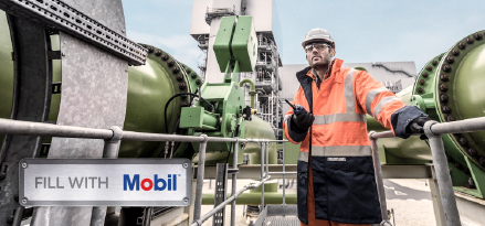 Worker in high-visibility protective clothing inspecting industrial equipment at a facility.